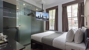 Ein modernes Hotelzimmer mit einem Bett, einem an der Wand befestigten Fernseher, einem Schreibtisch mit Fernbedienung und einem Fenster mit Vorhängen.