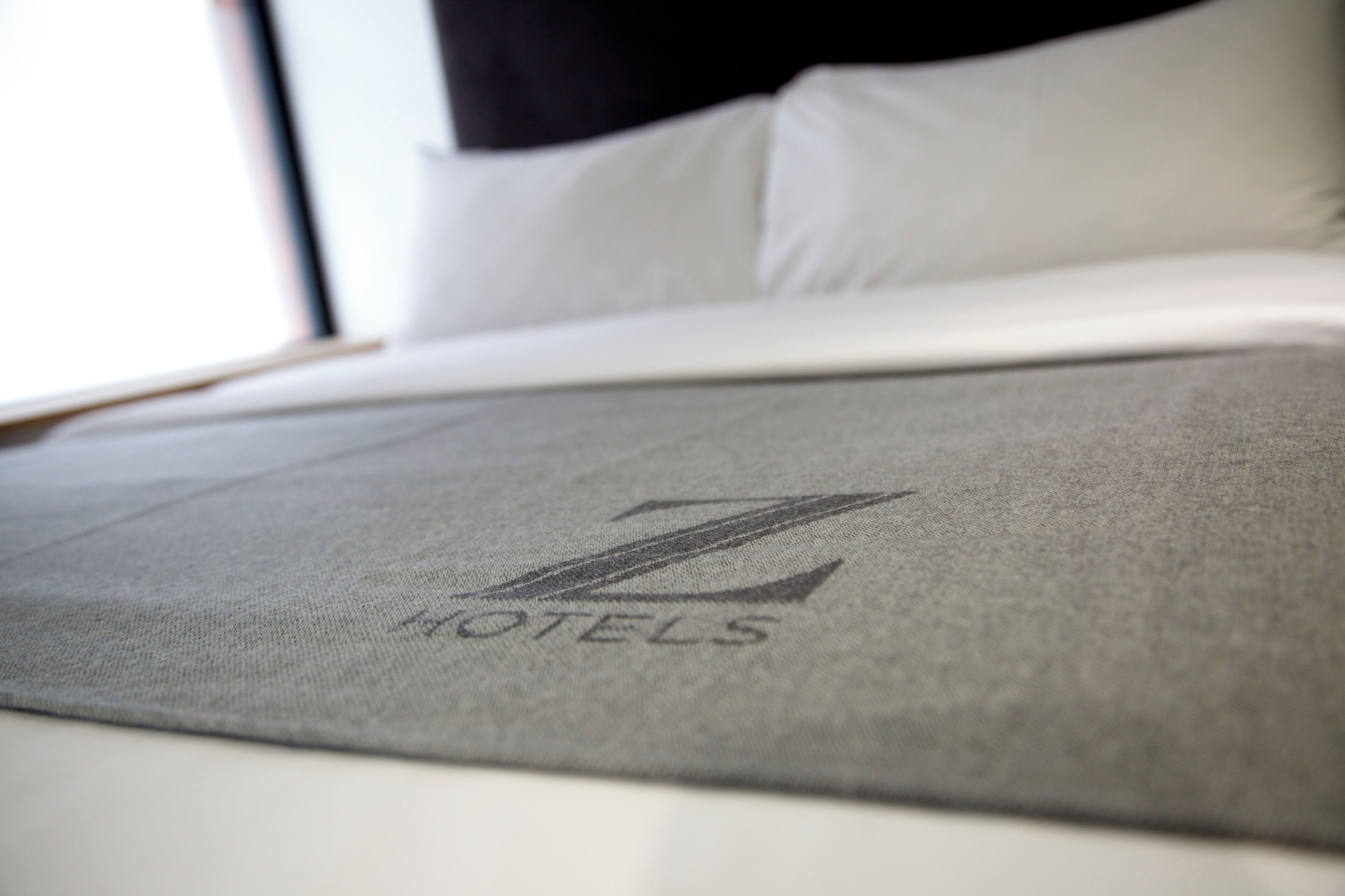 Un letto con copripiumino grigio e un cuscino con un logo.