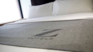 Un letto con copripiumino grigio e un cuscino con un logo.