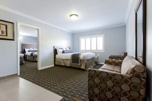 A hotel room with a bed, a sofa, a patterned rug, and a window. - Hollywood Palms Inn and Suites (Los Angeles)