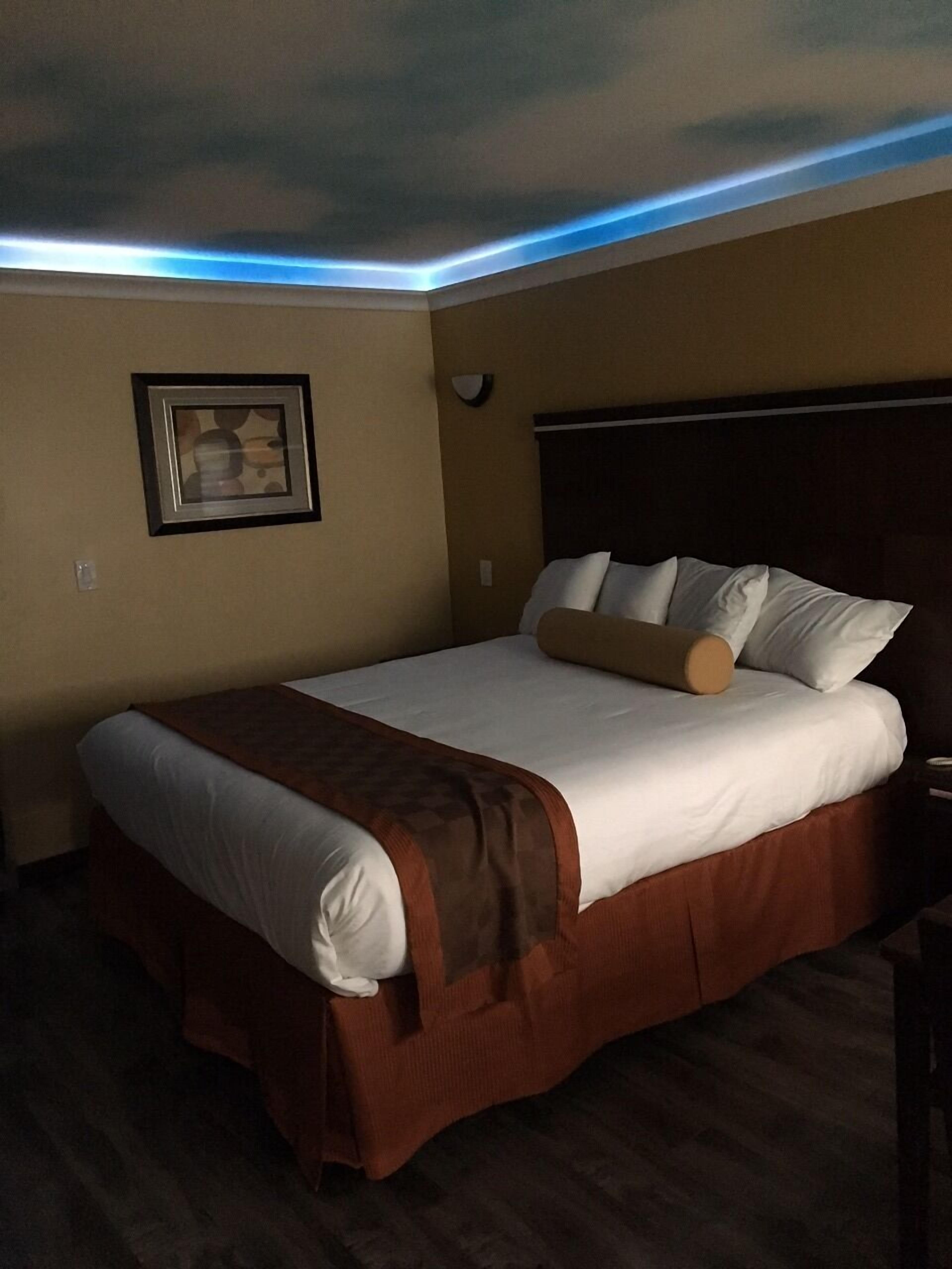 A hotel room with a large bed, a headboard, a framed picture on the wall, and a ceiling light.
