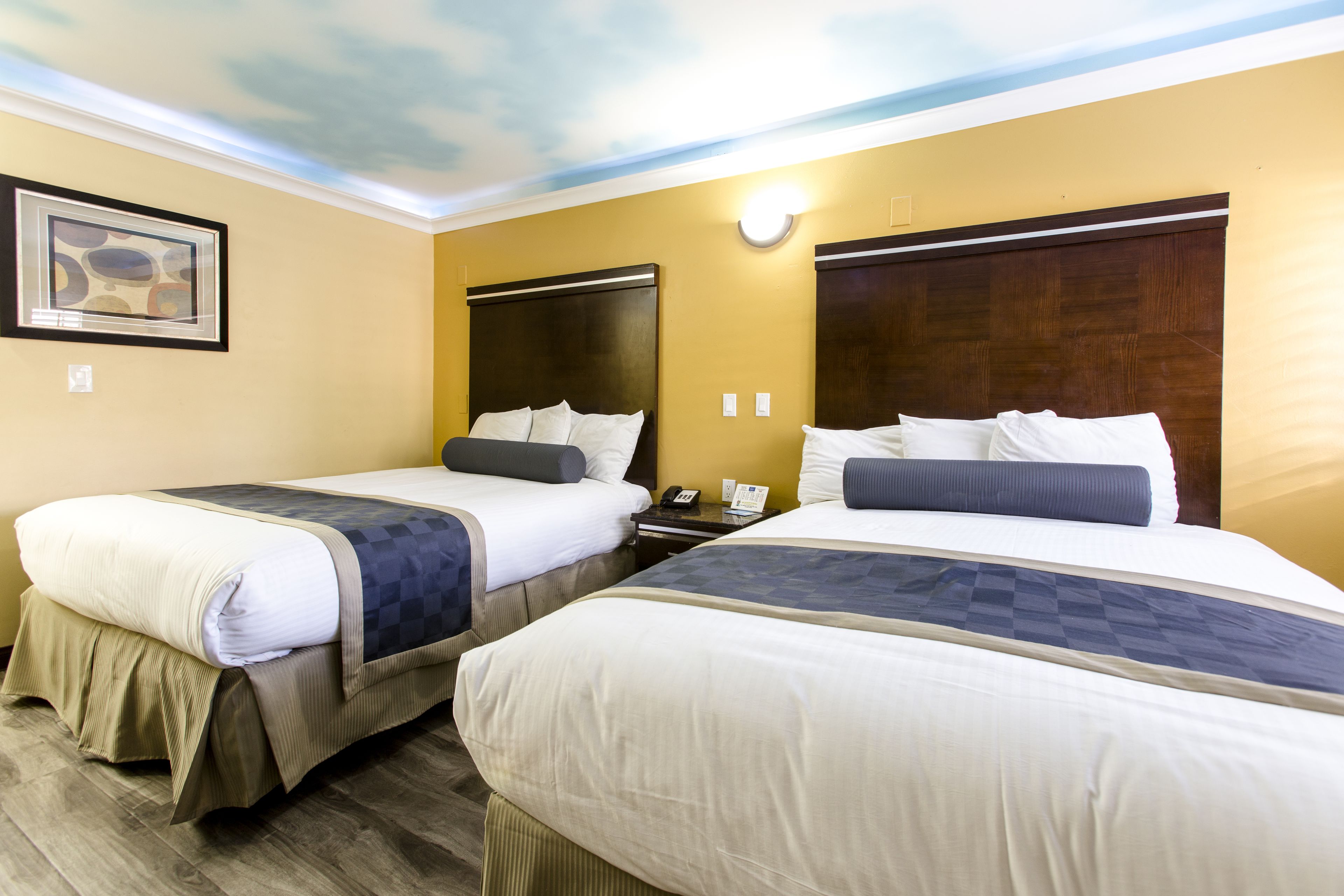 Habitación de hotel con dos camas, un cuadro en la pared y un techo con diseño de nubes.