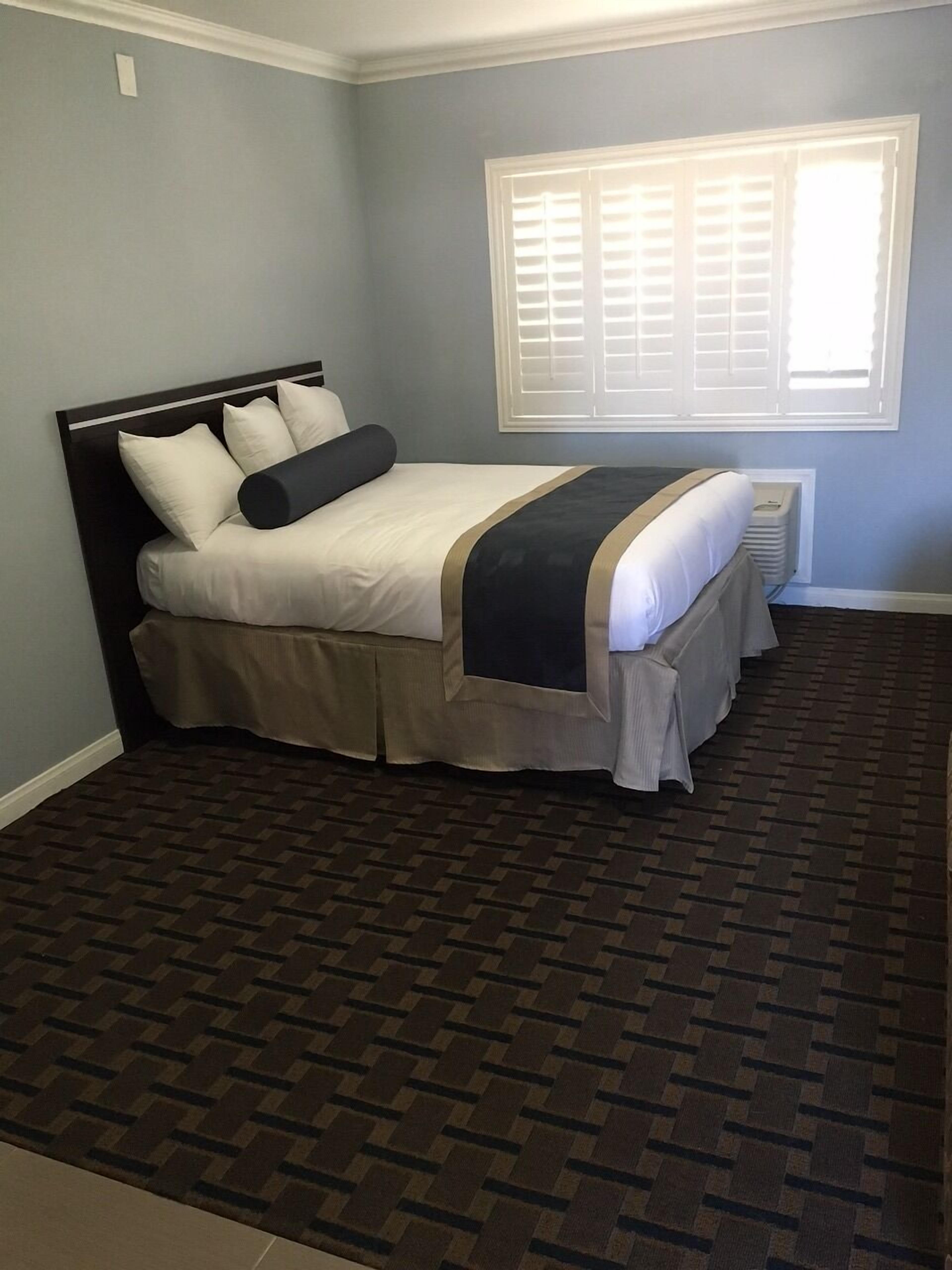 A bedroom with a bed, a window with blinds, and a patterned carpet.