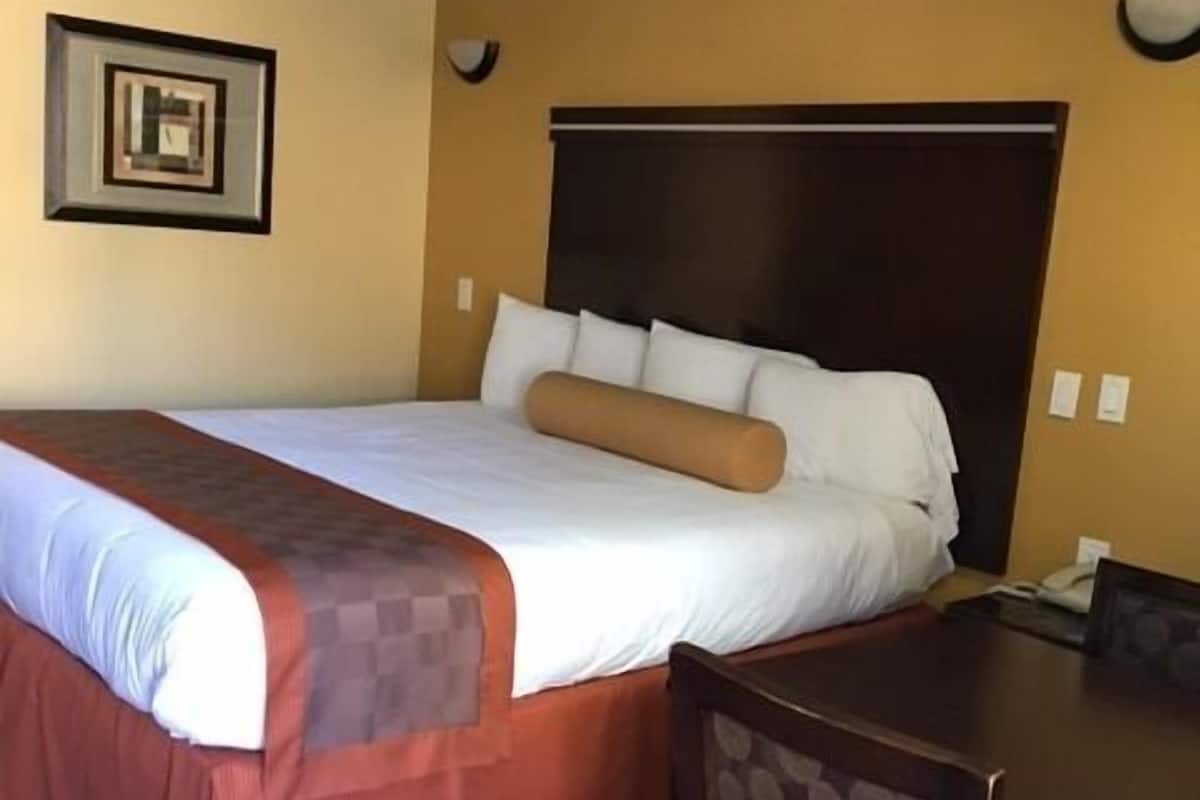 A hotel room with a large bed, a wooden headboard, a dining table with chairs, and a ceiling mural.