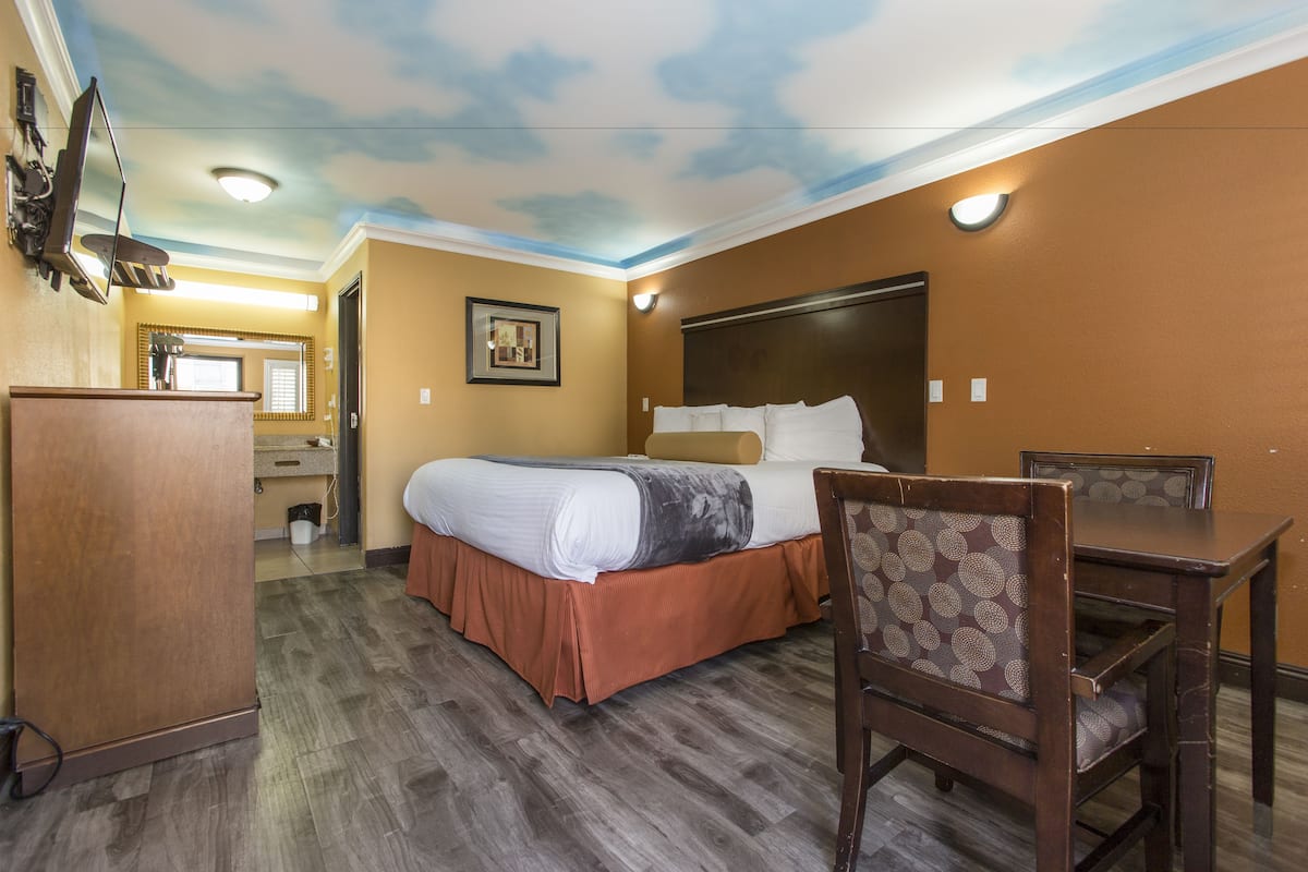 A hotel room with a bed, a desk, a chair, a dresser, and a ceiling with a cloud design.