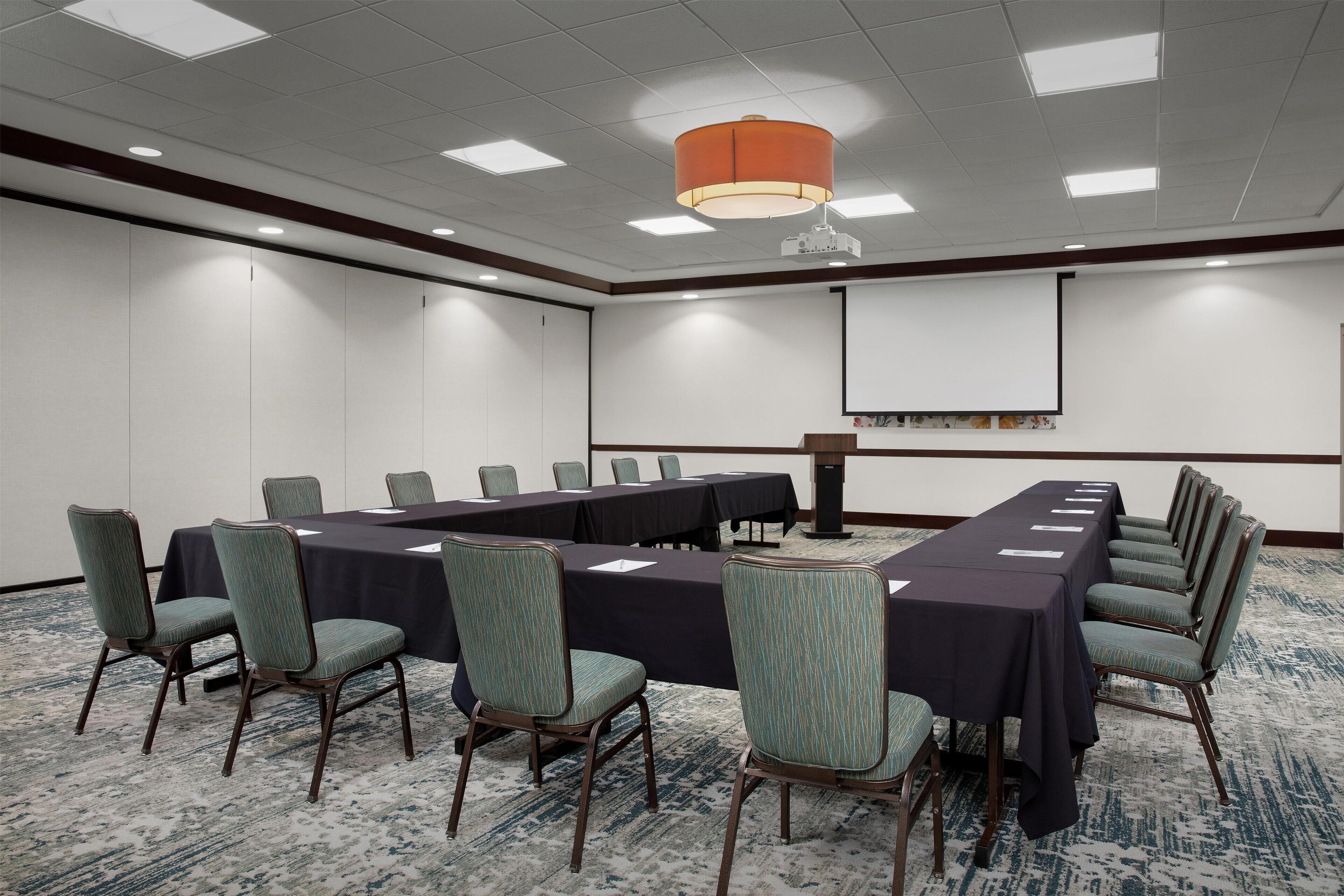 A conference room with a long table, chairs, a projector screen, and a carpeted floor.