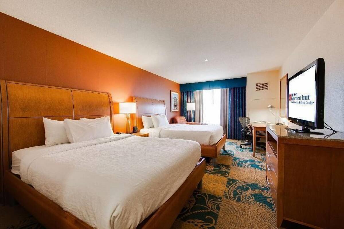 A hotel room with two beds, a desk, a television, and a carpeted floor.
