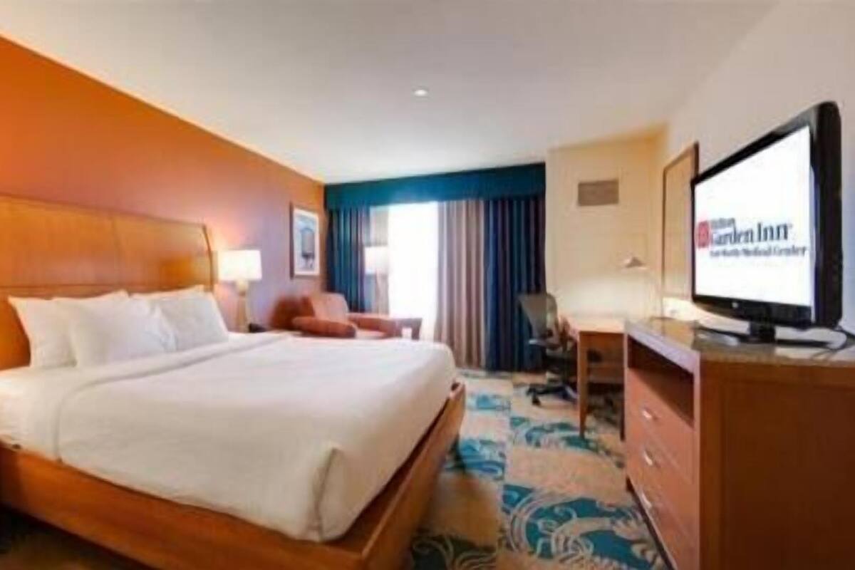 A hotel room with a bed, a desk, a chair, a television, and a window with curtains.
