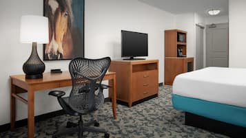 Ett hotellrum med en säng, ett skrivbord, en stol, en tv och en tavla på väggen.