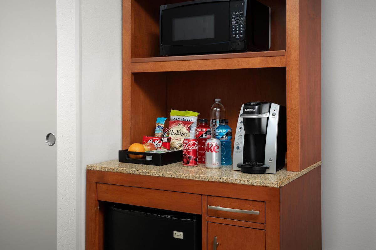 A kitchenette with a microwave, coffee maker, and various food and drink items.