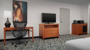 A hotel room with a bed, a desk with a lamp, a television, a wooden dresser, and a microwave.