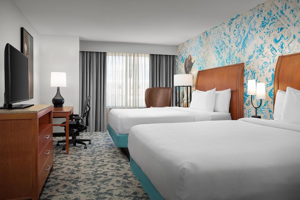 A hotel room with two beds, a desk with a television, a chair, and a lamp.