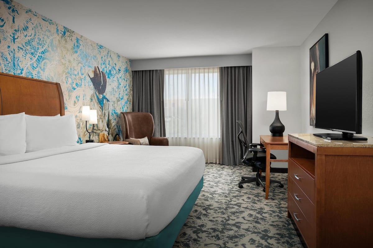 A hotel room with a large bed, a desk with a computer, a chair, a television, and a decorative wall.