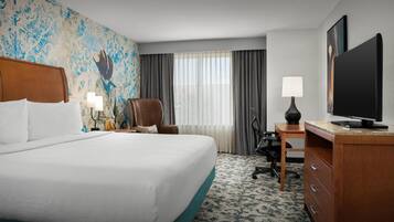 A hotel room with a large bed, a desk with a computer, a chair, a television, and a decorative wall.