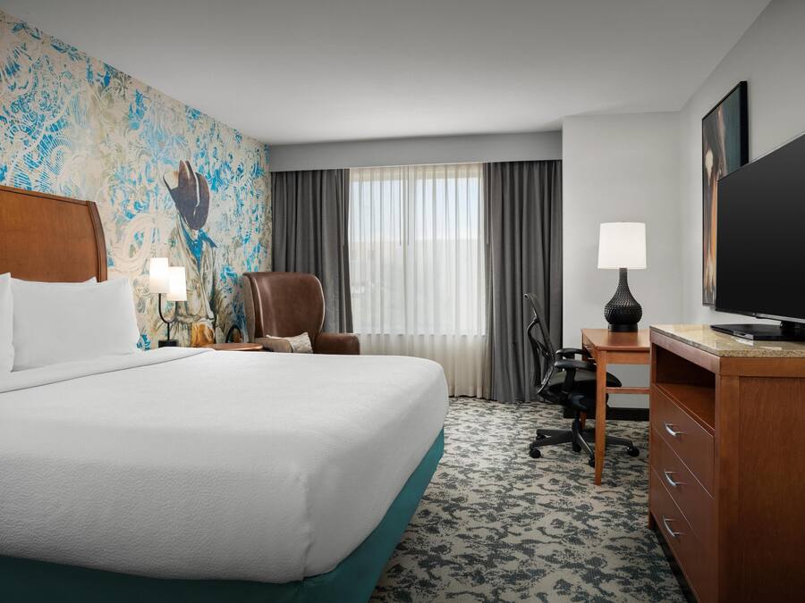 A hotel room with a large bed, a desk with a computer, a chair, a television, and a decorative wall.