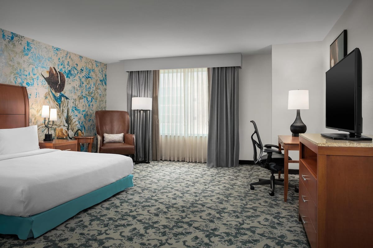 A hotel room with a bed, a desk, a chair, a television, and a window with curtains.
