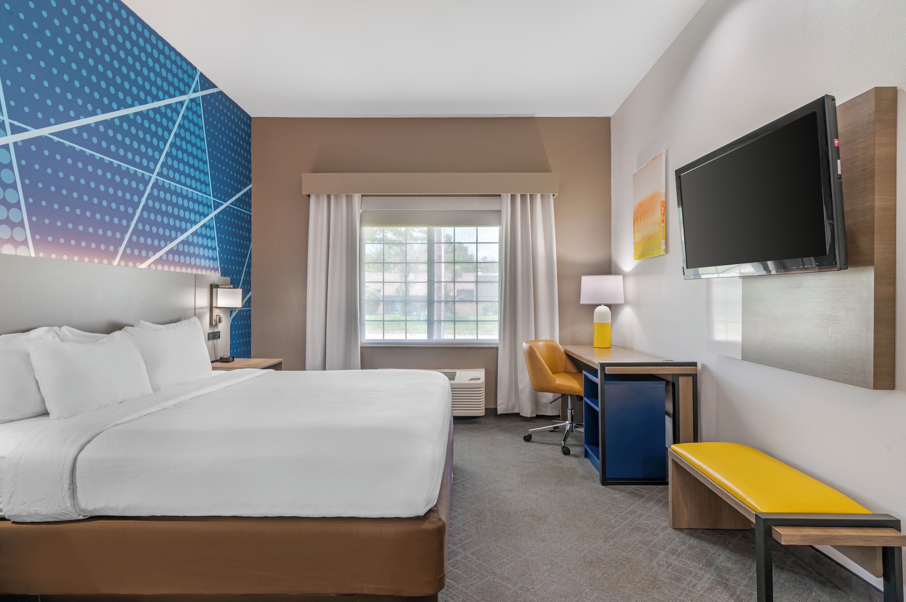 A hotel room with a bed, desk, chair, TV, and a window with curtains.