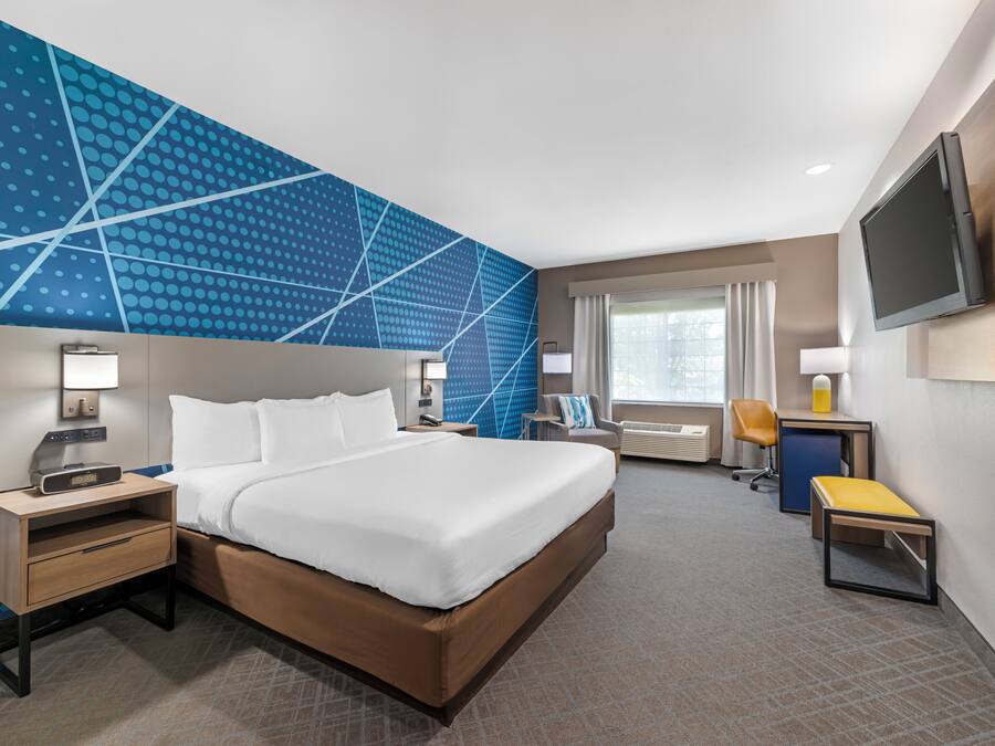 Une chambre d’hôtel avec un grand lit, un bureau avec une chaise, un téléviseur fixé au mur et une fenêtre avec des rideaux.