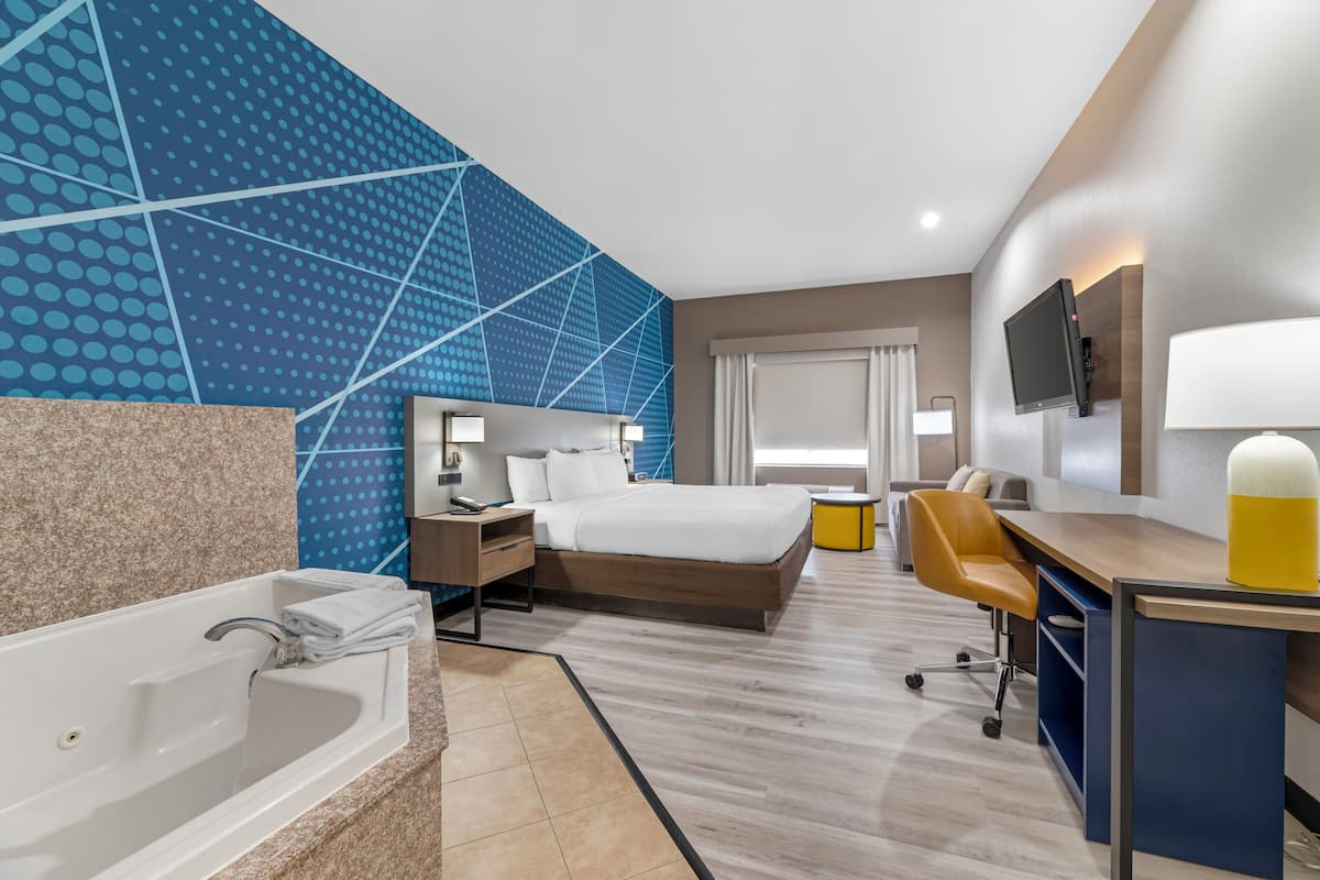 Habitación de hotel con una cama grande, un escritorio, una silla, un televisor y un baño con bañera, y una pared con diseño azulado.