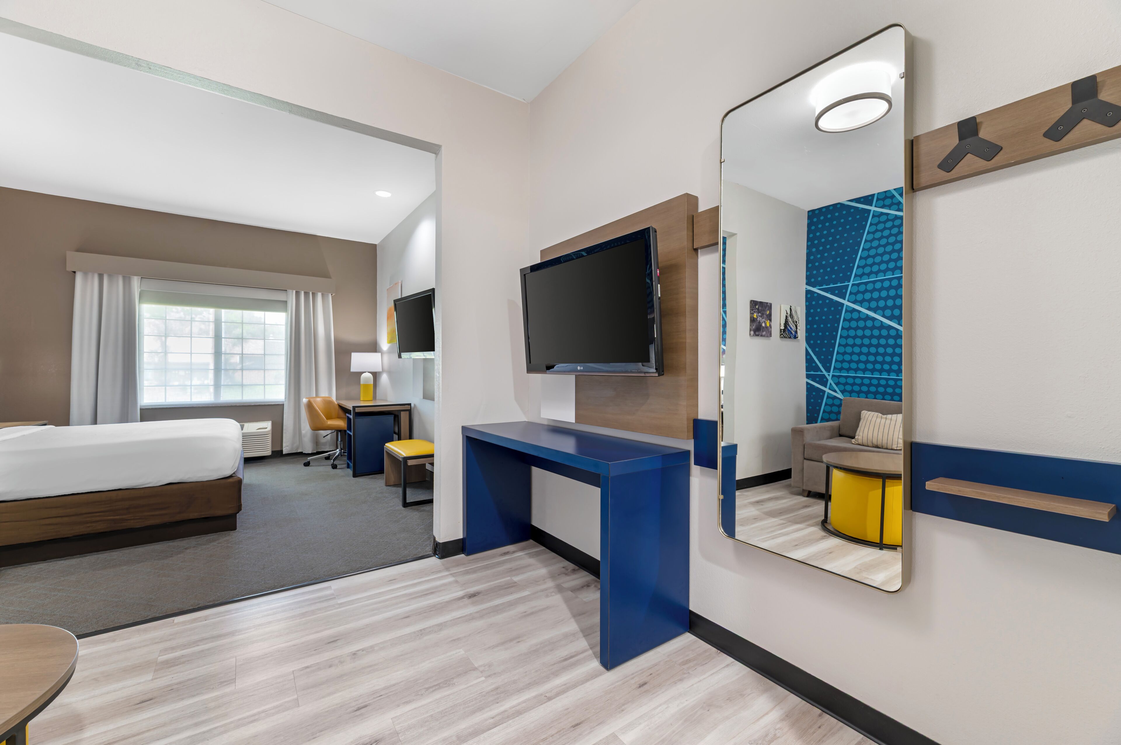 Habitación de hotel con cama, escritorio, televisión y un espejo grande.