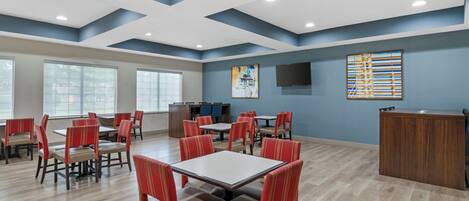 A spacious dining area with multiple tables and chairs, a wooden reception desk, and a large window providing natural light.