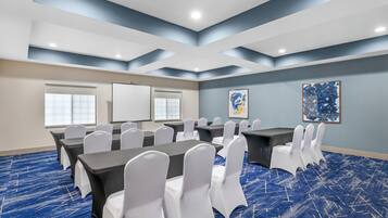 Ein Konferenzraum mit blauem Teppich, weißen Stühlen und einer Projektionsleinwand.