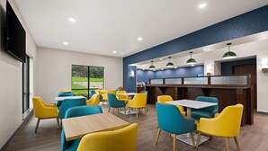 A modern dining area with yellow and blue chairs, wooden tables, and a counter with a blue accent wall. - Comfort Suites Hudson I-94 (Hudson)