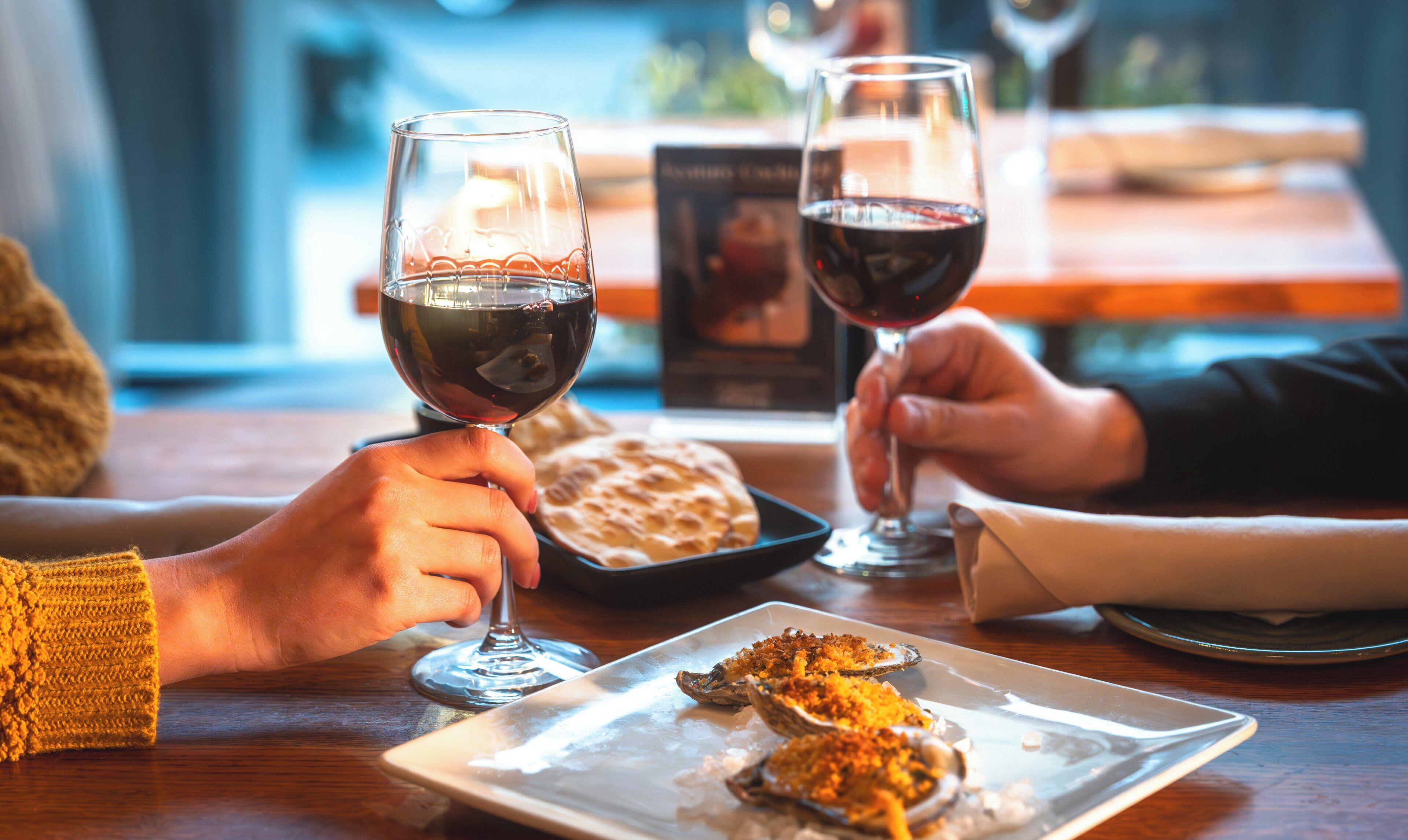 A dining table with a plate of oysters, two wine glasses, and a menu.