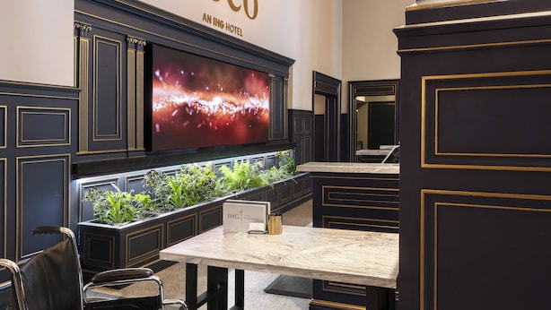 A modern hotel lobby with a large TV screen, a reception desk, and a decorative plant display.