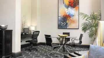 A conference room with a modern design, featuring a round table, black office chairs, a large abstract painting, and a potted plant.