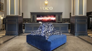 A luxurious hotel lobby with a large TV screen, a blue sofa, and a chandelier.