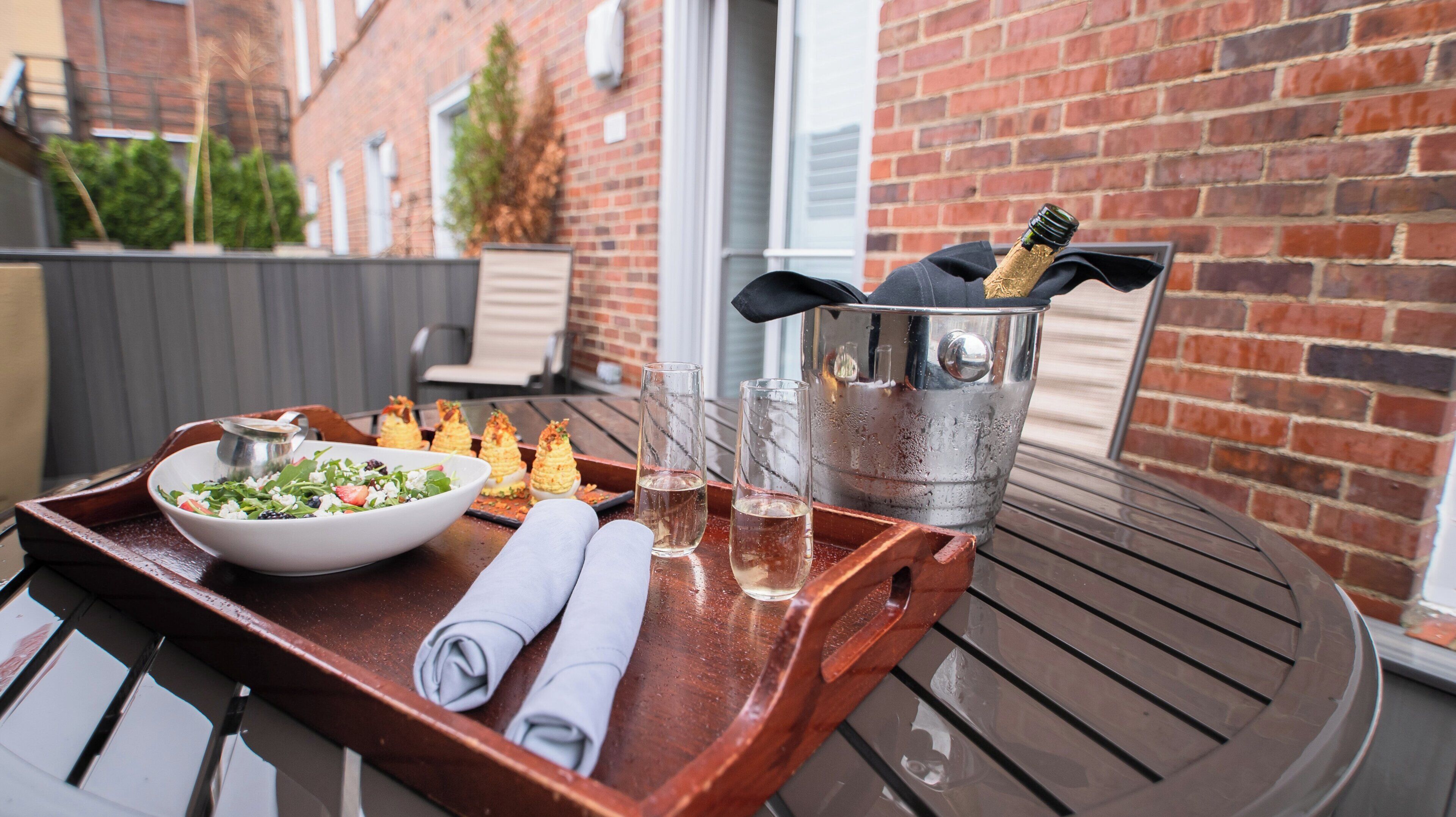 A table with a tray containing a salad bowl, two glasses of a clear liquid, a bottle of champagne, and a folded napkin.