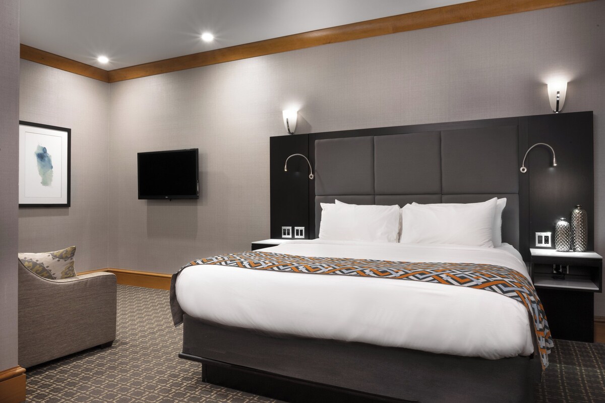 A modern hotel room with a large bed, a flat-screen TV, and a bedside table with a lamp.