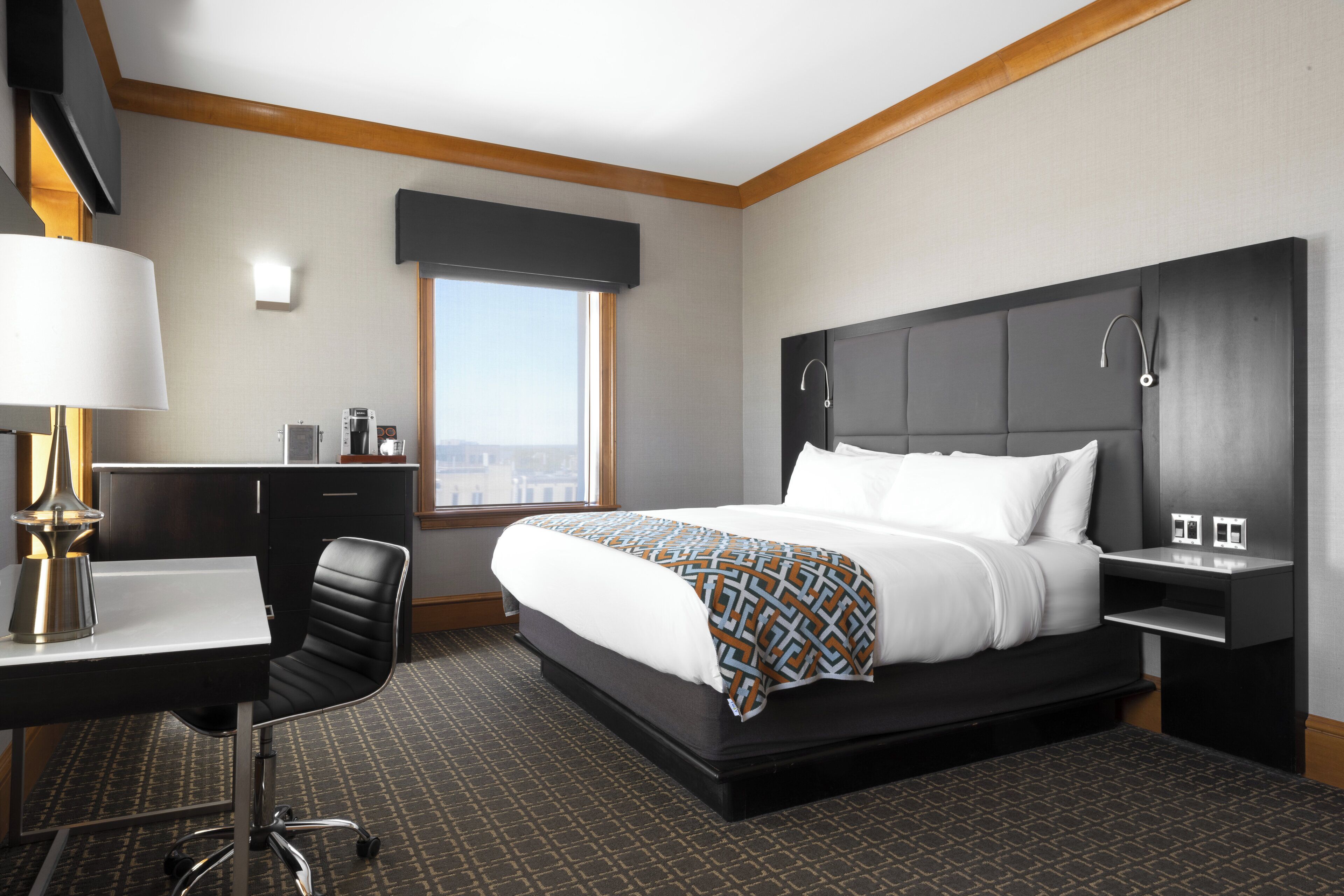 Une chambre d’hôtel équipée d’un lit, d’un bureau, d’une chaise et d’une fenêtre donnant sur la ville.