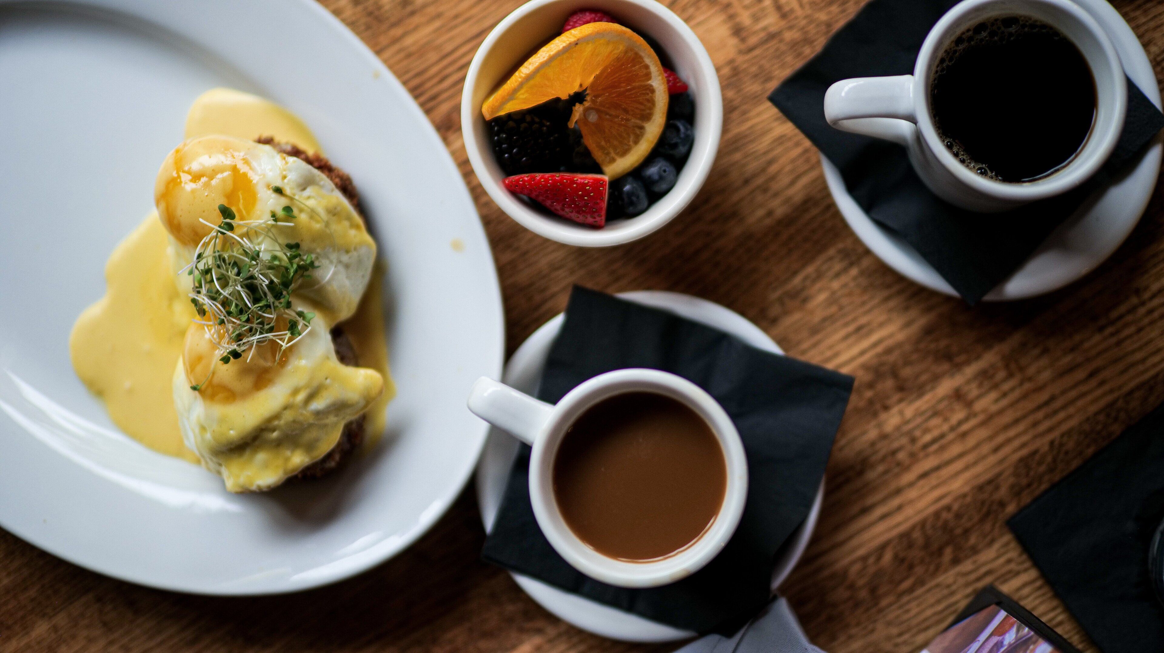 Ein Frühstückstisch mit Eggs Benedict, einer Tasse Kaffee und einer Schüssel Beeren.
