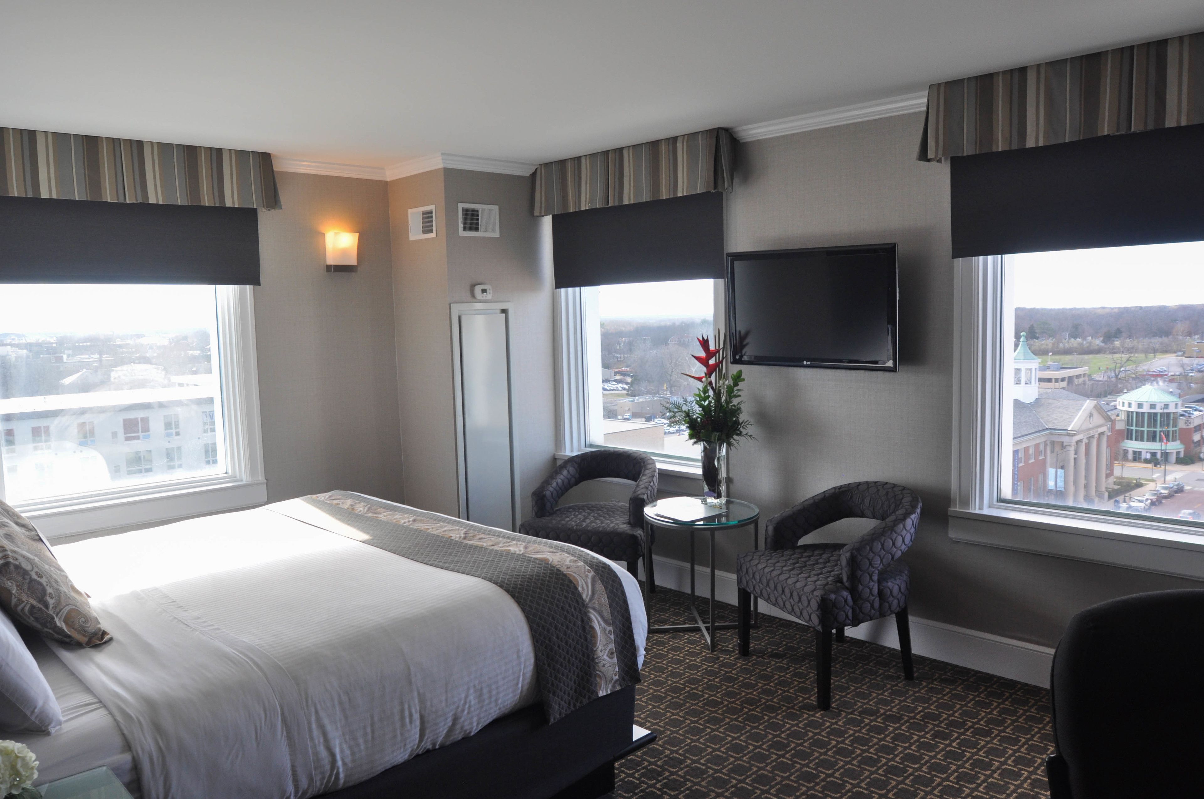 Una habitación de hotel con una cama grande, dos sillones, una mesita, un televisor y una ventana con vistas a la ciudad.