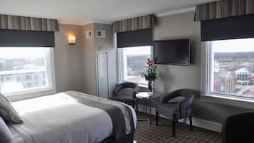 Una habitación de hotel con una cama grande, dos sillones, una mesita, un televisor y una ventana con vistas a la ciudad.