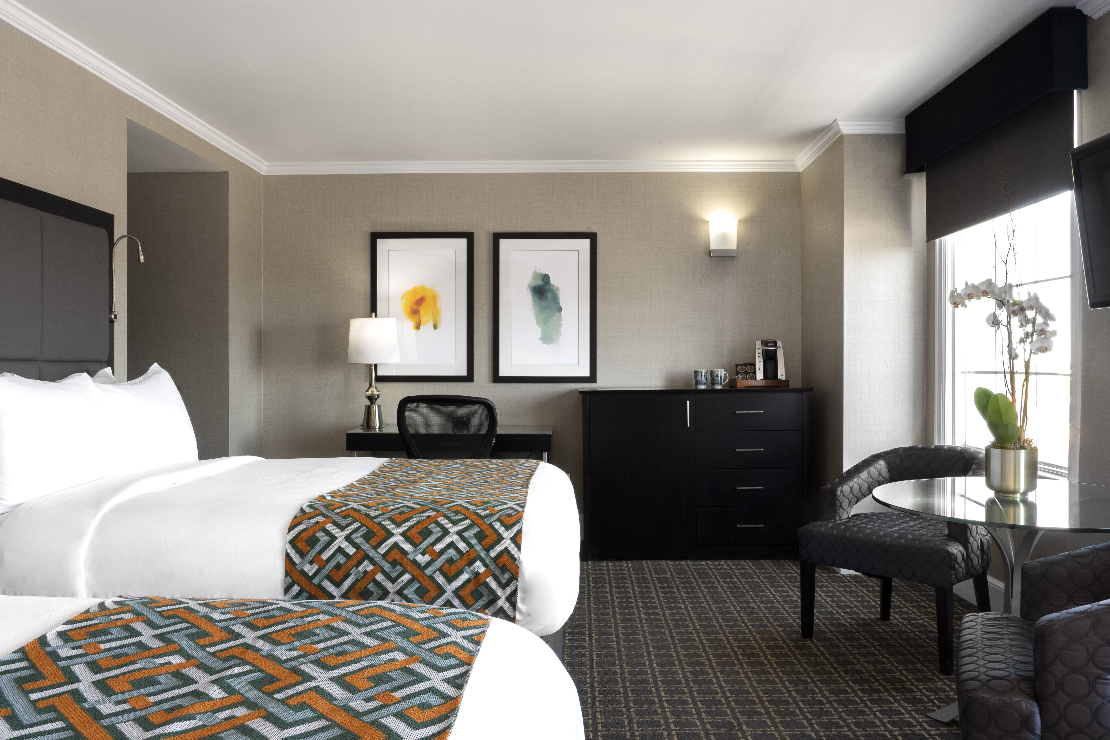 A hotel room with two beds, a desk, a chair, a dresser, and a window with a plant.