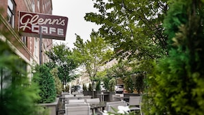 An outdoor cafe area with tables and chairs, surrounded by greenery and a sign for 'Glenn's Cafe'.