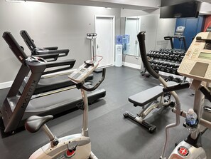 Une salle de sport équipée de tapis de course, de vélos elliptiques et d’haltères.