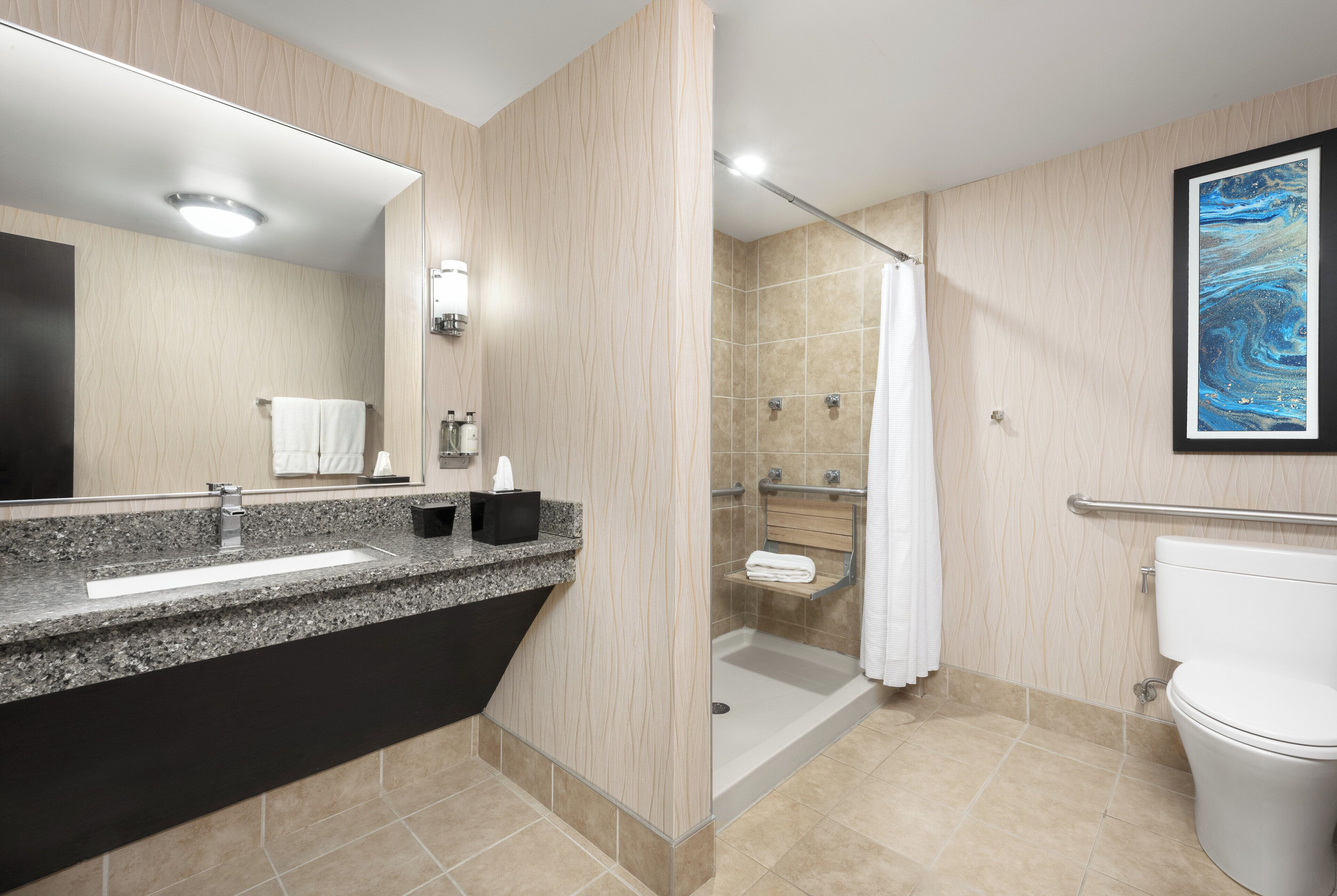 Een moderne badkamer met een granieten werkblad, een grote spiegel, een douche met glazen deur en een toilet.
