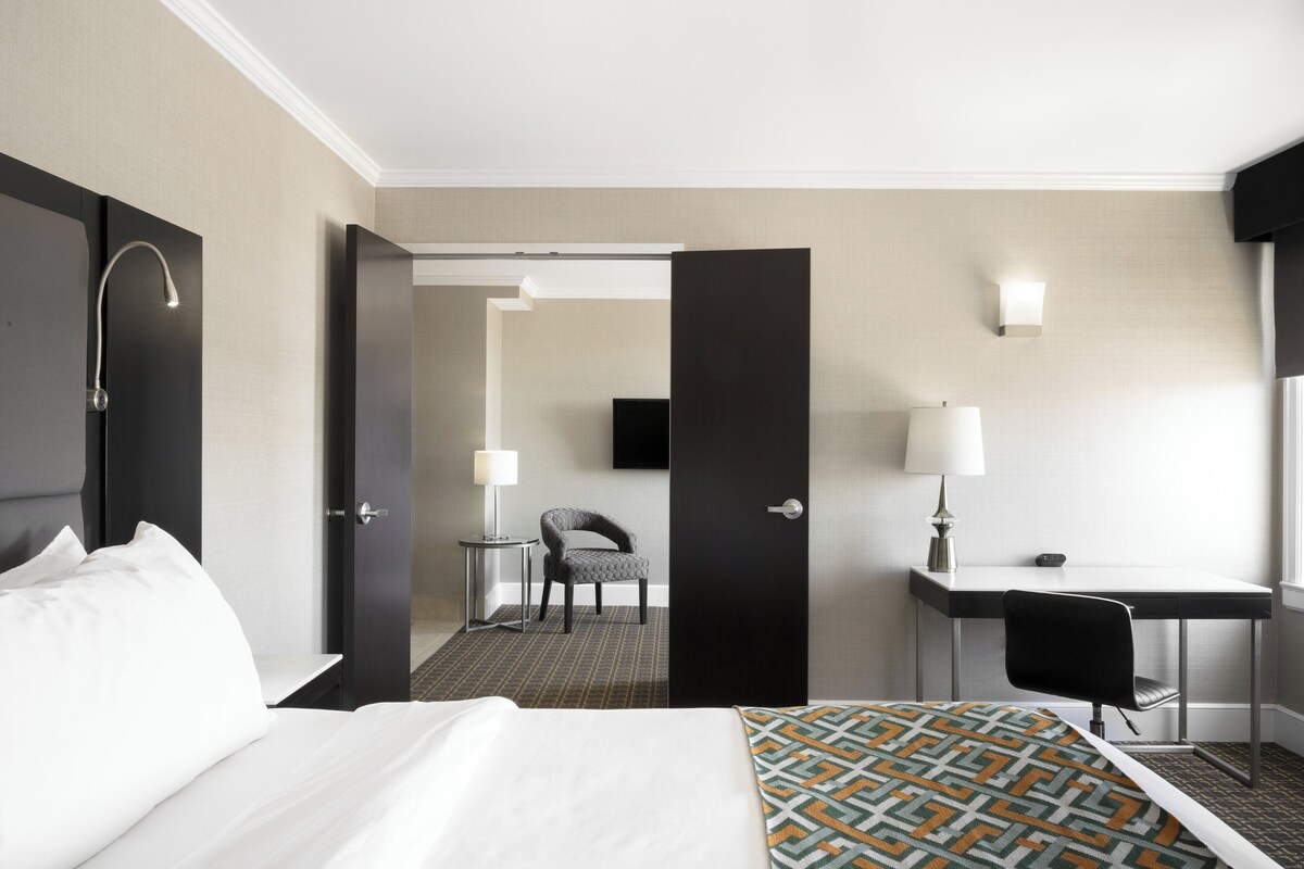 A hotel room with a bed, a desk, a chair, a TV, and a door.