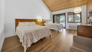 A bedroom with two beds, wooden flooring, a sloped ceiling, and a large window. - Amador Hotel (Pioneer)