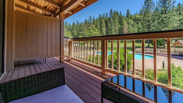 A wooden deck with a view of a swimming pool and forest. - Amador Hotel (Pioneer)