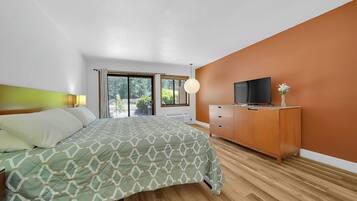 A bedroom with a bed, a TV on a wooden cabinet, and a window with curtains.