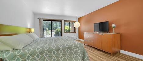 A bedroom with a bed, a TV on a wooden cabinet, and a window with curtains.