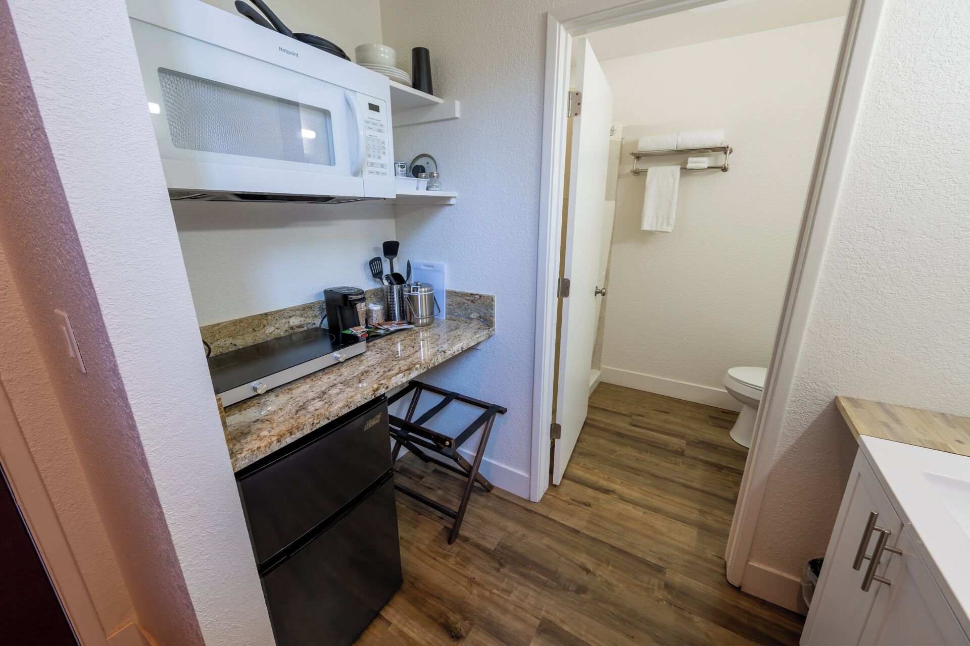 Una cocina compacta con microondas, cafetera y un lavamanos pequeño.