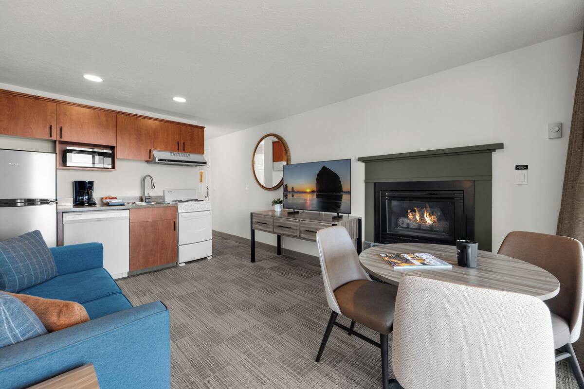 A modern kitchen with a dining area, a fireplace, and a living room with a sofa and chairs.