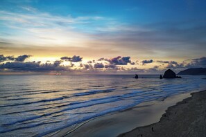 A beach with waves, a sunset, and distant rock formations. - The Wayside Inn (Cannon Beach)