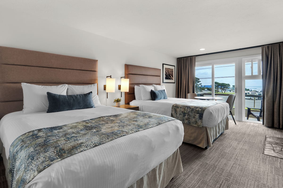 A hotel room with two beds, a balcony with a view, and a small table.